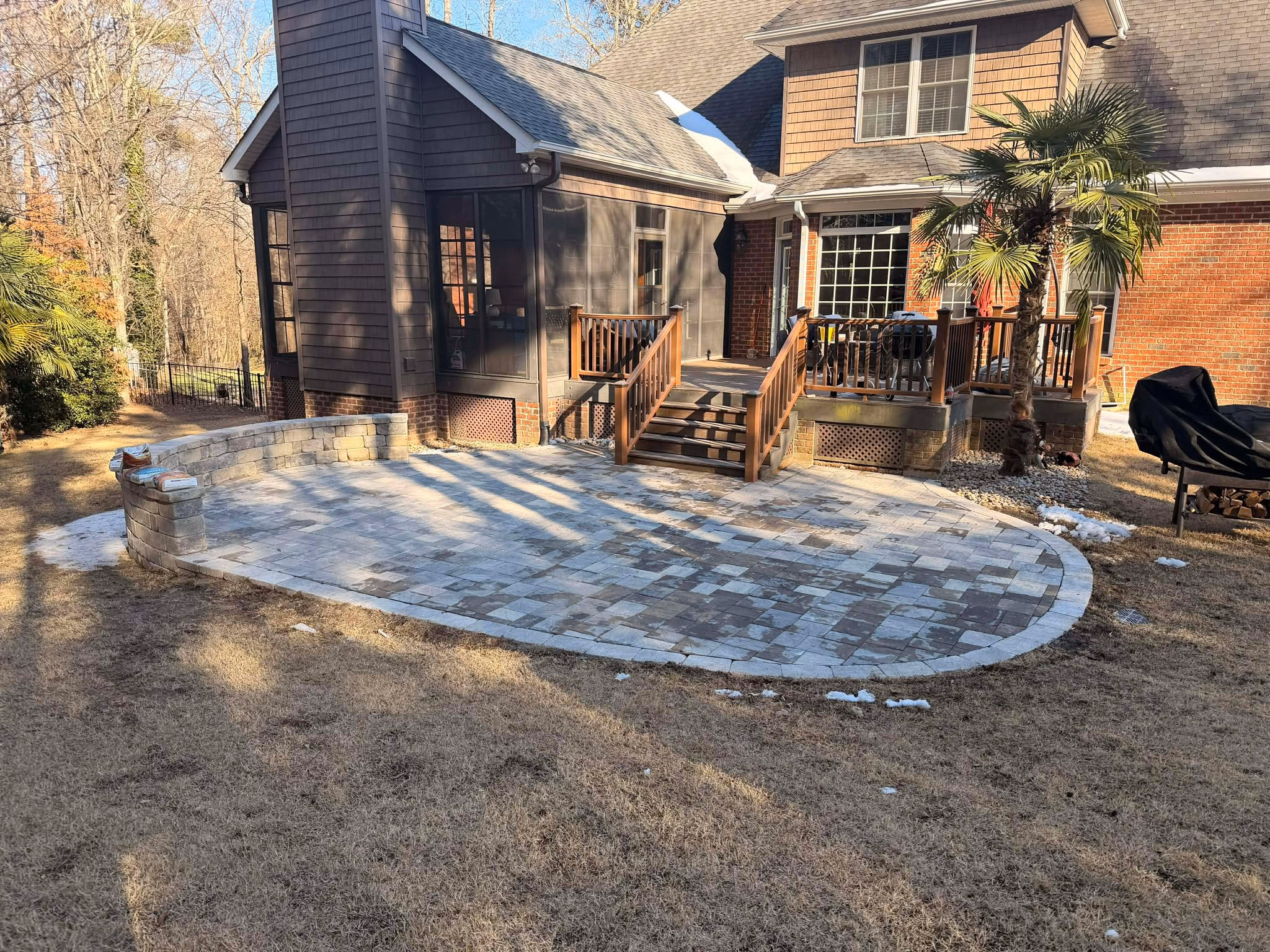 Finished paver patio behind a home with a wooden deck and screened porch above it.
