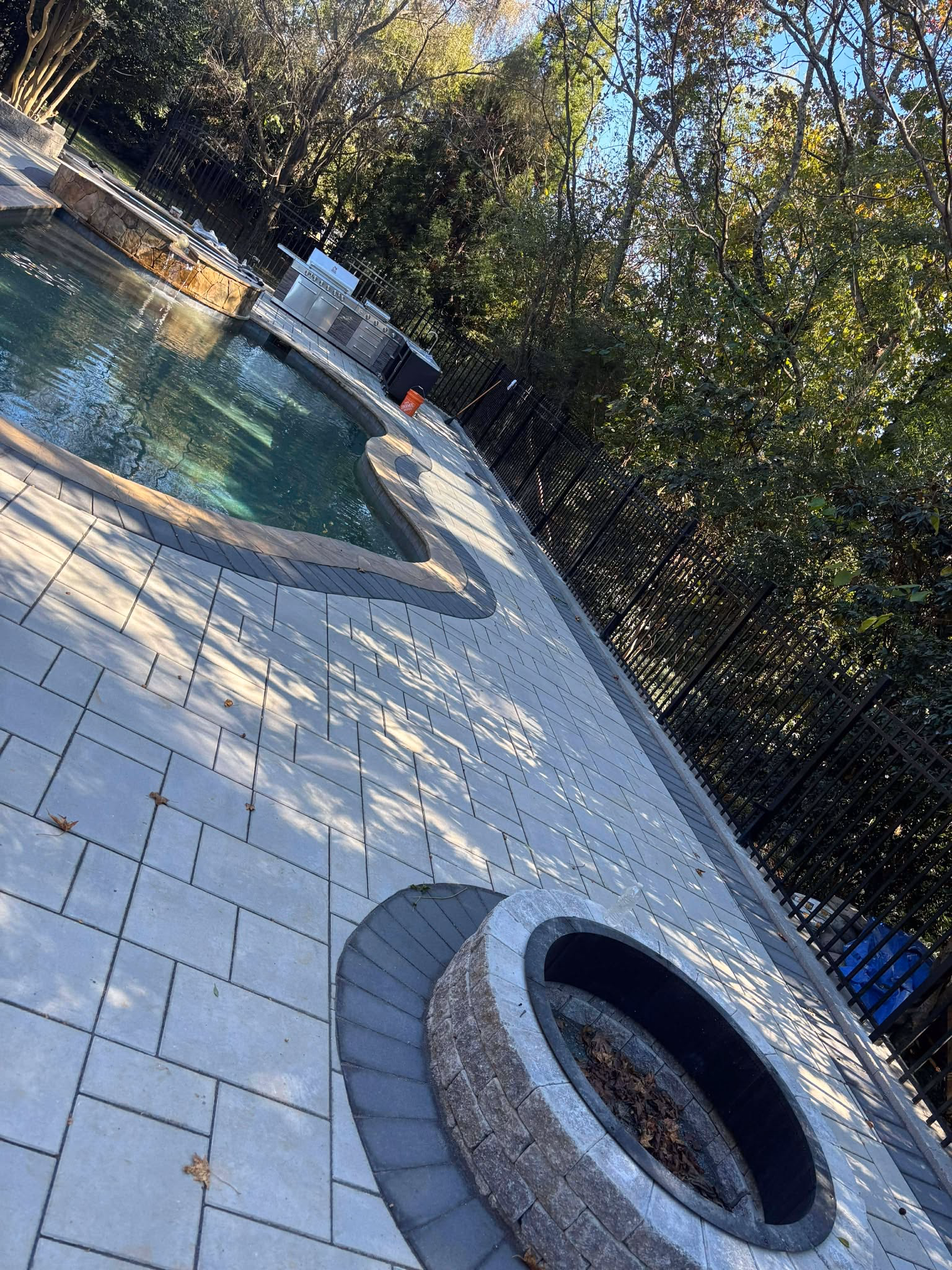 Paver pool deck with a built-in fire pit set into the paving beside the water.
