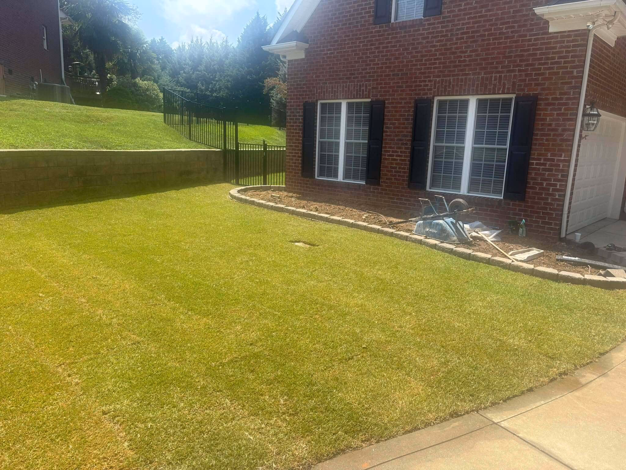 Established lawn running down a slope beside a brick home, with a stone border along the bed.