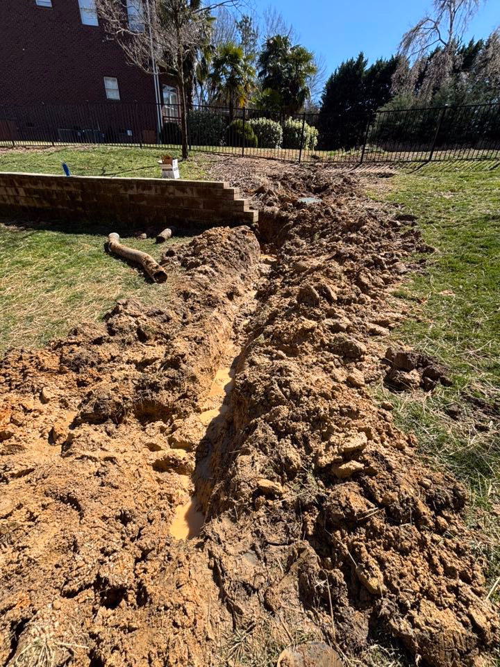 Open drainage trench cut across a lawn with soil piled beside it.
