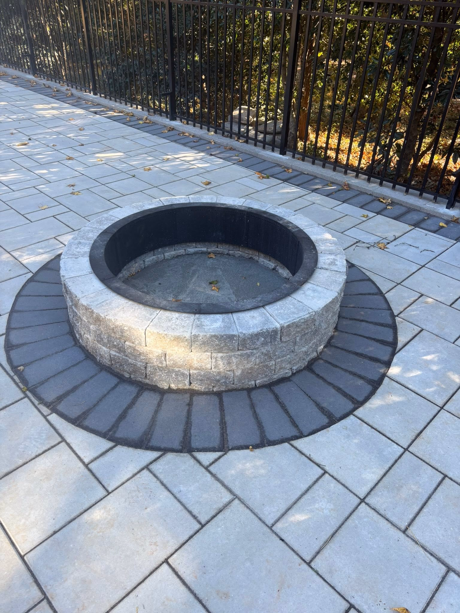 Circular stone fire pit built into a gray paver patio with a capped top course.
