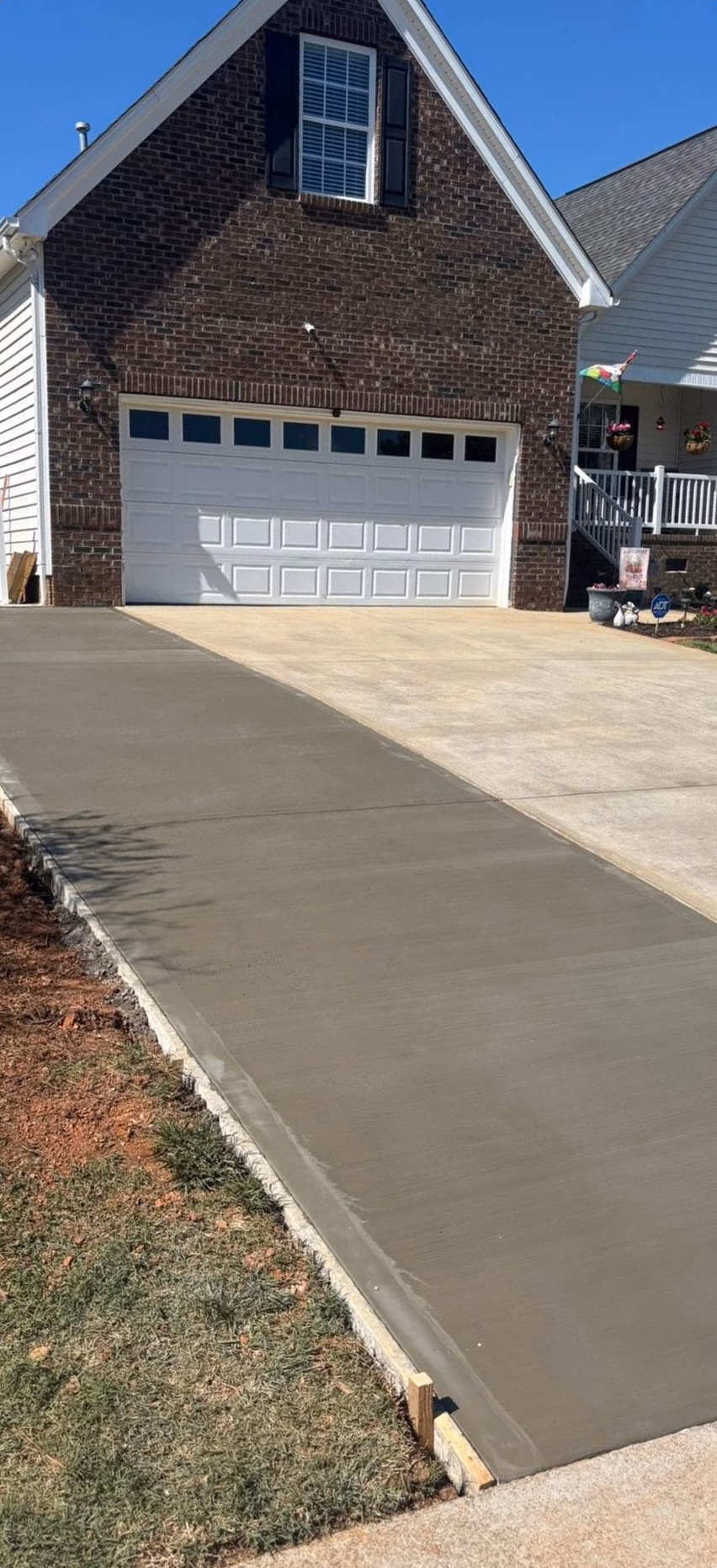 Freshly poured concrete driveway curving up to a two-car garage on a brick home.
