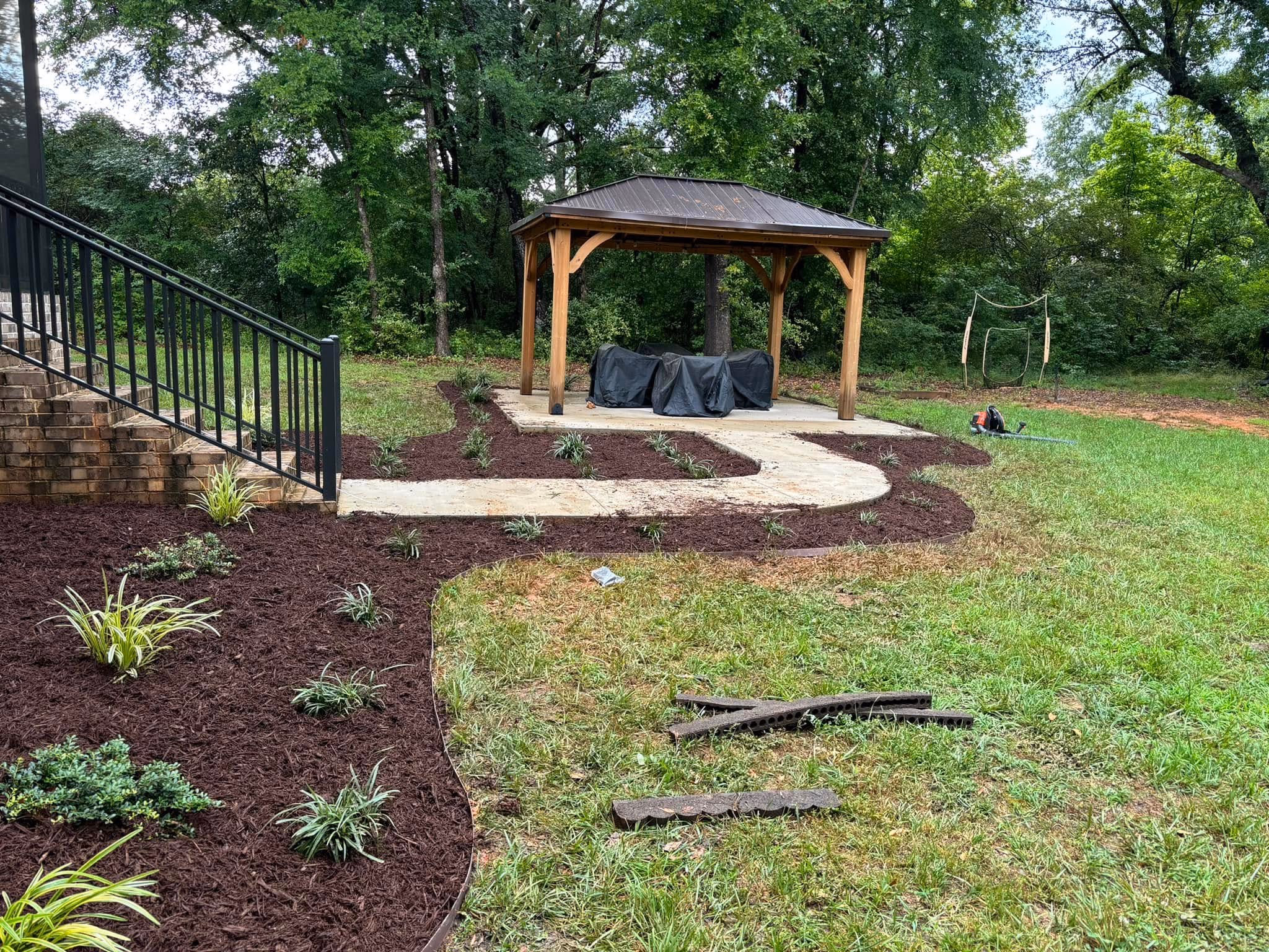 Curved paver path through fresh mulch beds leading to a wooden gazebo.