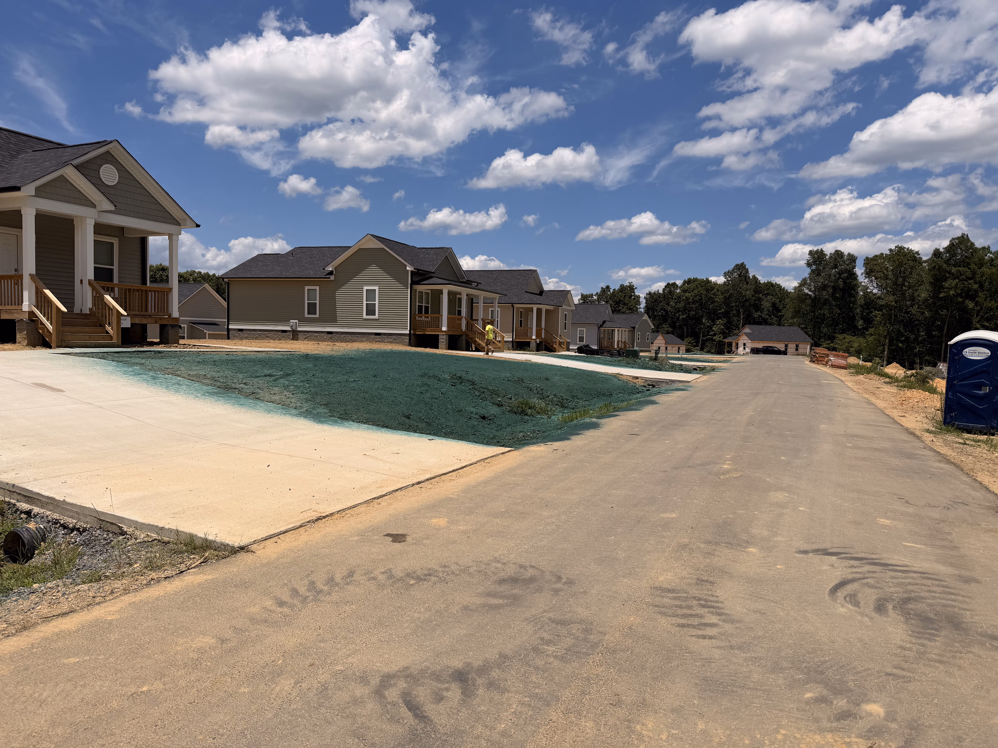 Green hydroseed slurry sprayed across a graded new-construction lot in front of newly built homes.