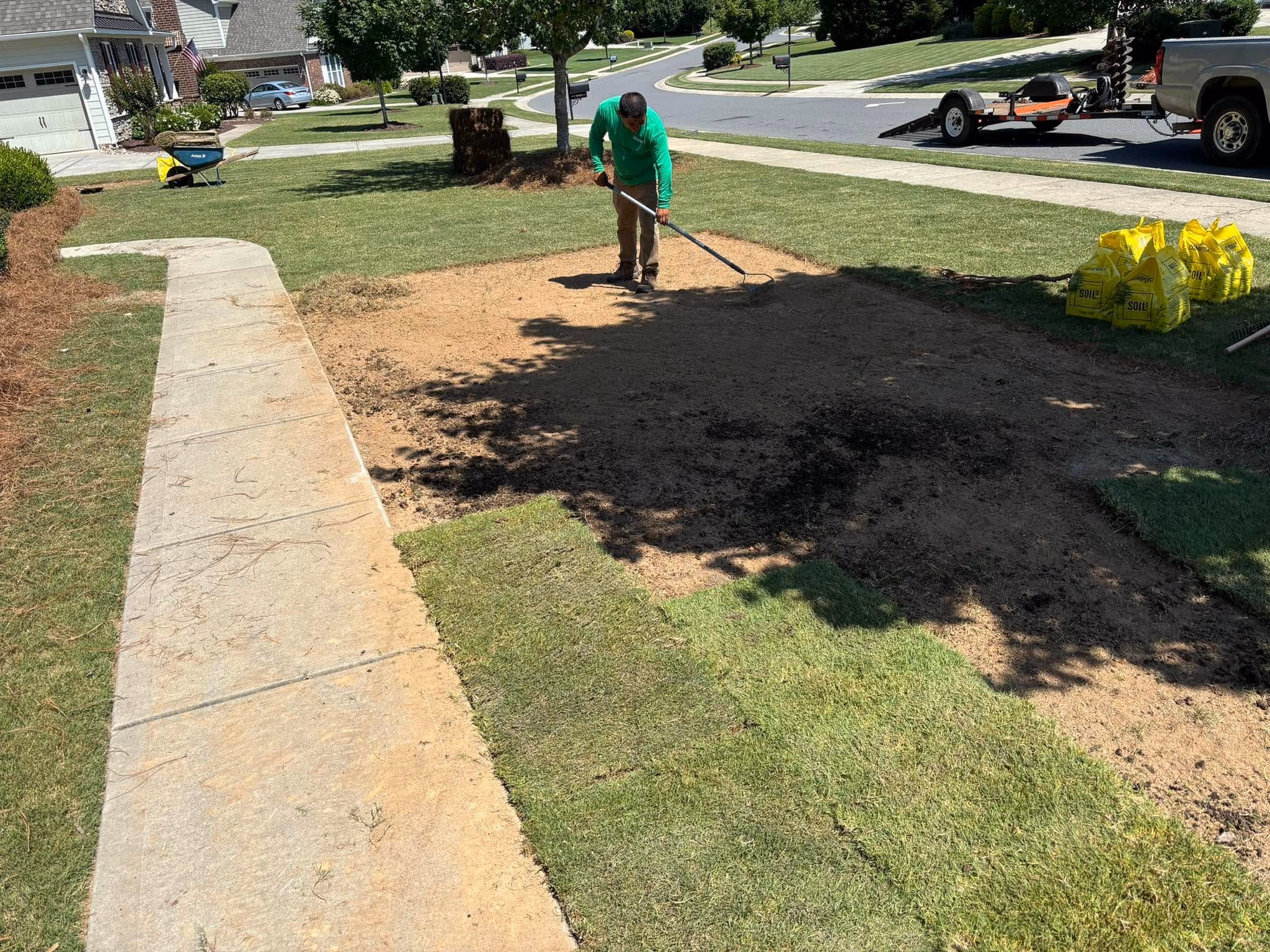 Crew raking bare soil smooth across a front yard before seeding.