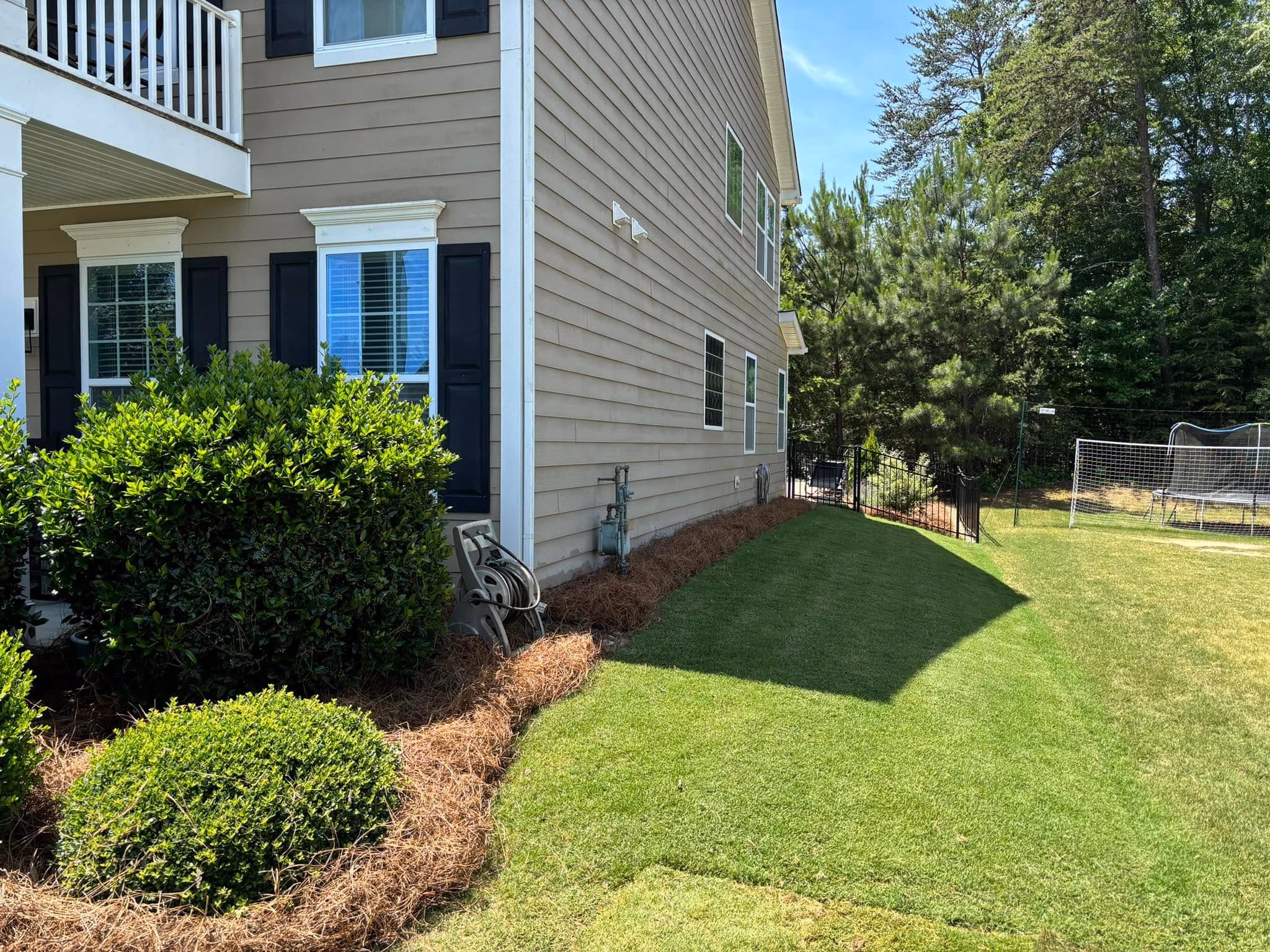 Fresh green sod laid in a strip along the side of a brick house next to a mulched bed.