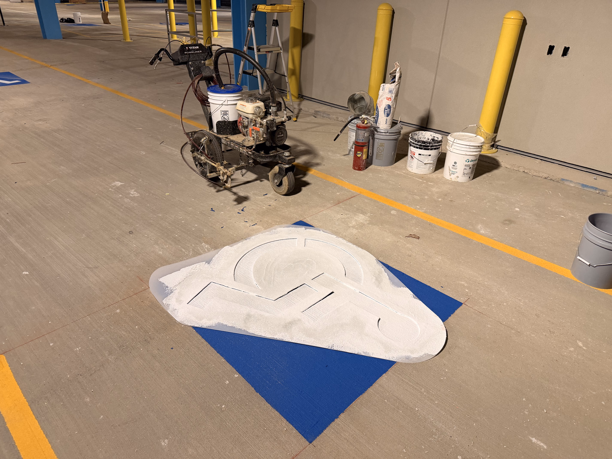 Line striping machine and stencil equipment staged on a parking deck during marking work.