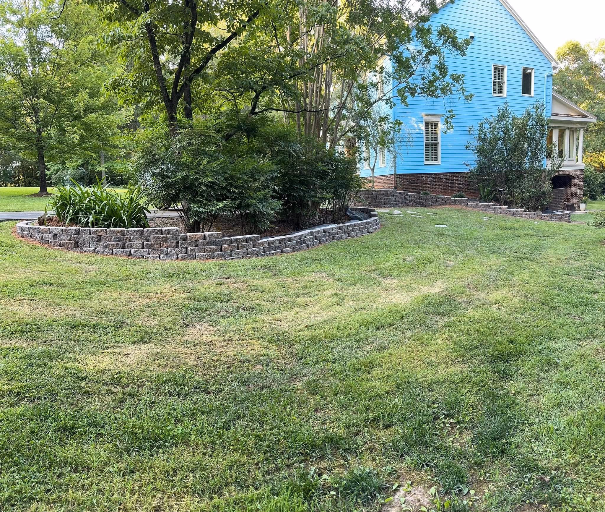 Long stacked stone retaining wall holding a graded slope beside a mown lawn.