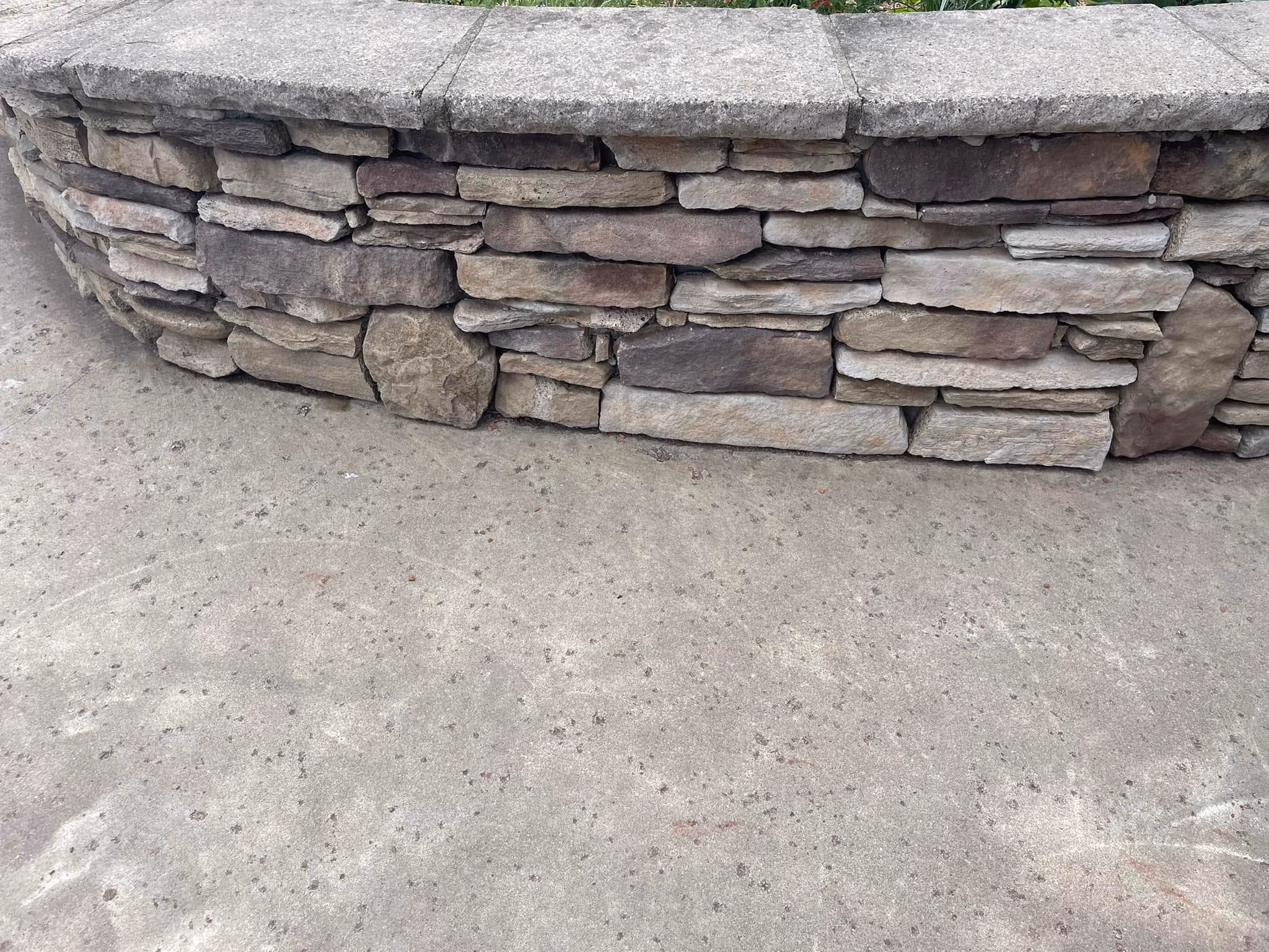 Stacked stone retaining wall curving beside a concrete apron.
